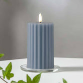 Kék Stripe LED gyertya dekor pohárban elhelyezve, meleg fényben világítva, zöld növényi elemekkel körülvéve, meghitt beltéri hangulatban.